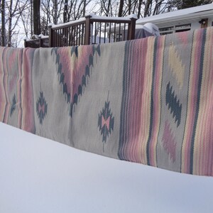 May include: A gray, pink, and yellow striped woven rug with a geometric pattern hangs on a clothesline in the snow.