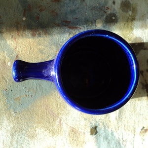 May include: A deep blue ceramic mug with a handle. The mug is empty and the inside is visible.
