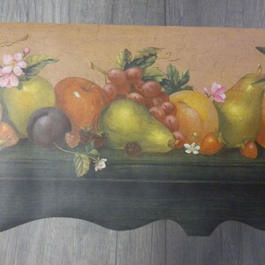 May include: A decorative wallpaper border featuring a still life of various fruits. The design includes apples, pears, grapes, and plums, with pink blossoms and green leaves. The color palette includes shades of green, red, yellow, and brown.