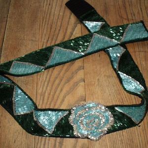 May include: A green and blue beaded belt with a large, round, silver and blue beaded buckle.