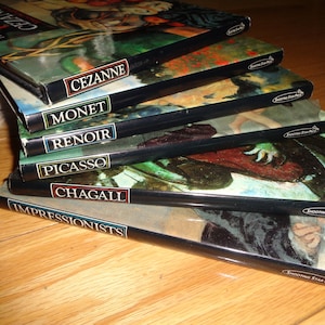 May include: A stack of six hardcover books about famous artists, including Cezanne, Monet, Renoir, Picasso, Chagall, and Impressionists. Each book features a colorful image on the cover.