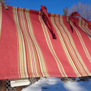 May include: Red, white, and beige striped fabric valance with a herringbone pattern. The valance has ties on each end and is hanging on a clothesline. The tag reads "Made in China".