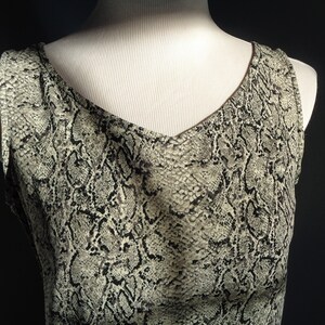 May include: A sleeveless top with a snakeskin print in shades of brown and beige. The top has a V-neckline and a relaxed fit.