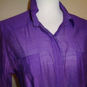 May include: A long-sleeved, purple button-down shirt made of a sheer, textured fabric.