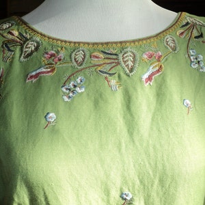 May include: A sleeveless green dress with a floral embroidered neckline. The embroidery is in shades of blue, red, and white.
