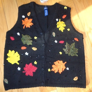 May include: Black button-up sweater vest decorated with colorful embroidered leaves in shades of orange, yellow, red, and green. The vest also features small white star-shaped accents and black beads.