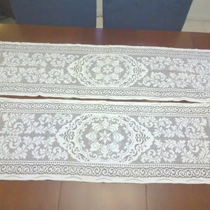 May include: Two white lace table runners with a floral pattern. The runners have a scalloped edge and are made of delicate lace.