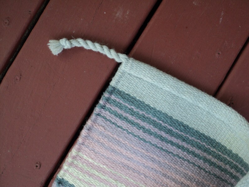 May include: A woven rug with a fringe edge. The rug has stripes of pink, light green, gray, and white.