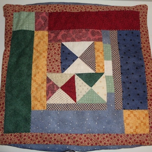 May include: A square patchwork pillow with a red, blue, green, and yellow geometric pattern. The pillow has a brown border with a floral design.