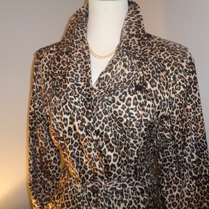 May include: A leopard print trench coat with a wide collar and a matching belt. The coat features a classic design with a brown, black, and tan spotted pattern. The coat is displayed on a mannequin.