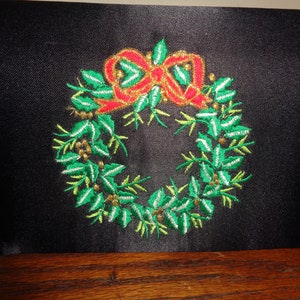 May include: Black clutch with an embroidered Christmas wreath design. The wreath features green leaves, gold berries, and a red bow. The clutch has a small black strap.