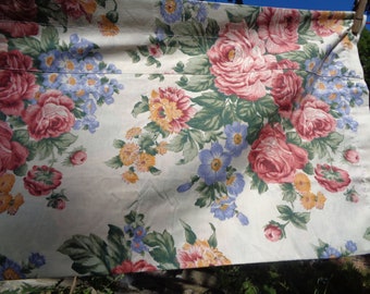 May include: A white fabric with a floral pattern featuring pink, red, blue, and yellow roses, and green leaves.