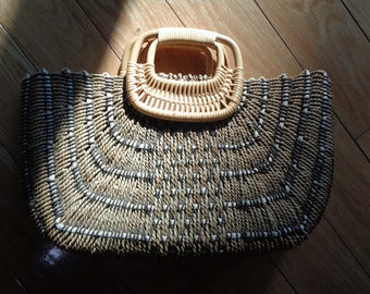 Pode incluir: Uma bolsa de palha tecida com um padrão natural marrom e branco. A bolsa tem uma única alça feita de palha tecida.