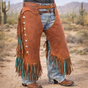 May include: Brown leather chaps with star-shaped studs and turquoise fringe. The chaps are worn over blue jeans and a brown leather belt. A western-themed fashion item.