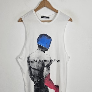 May include: A white sleeveless t-shirt featuring a graphic print of a figure with a blue head and a red arm. The text SAVAGE SCIENCE FICTION is printed across the back of the figure. The shirt has a black neck label with the text RAF.