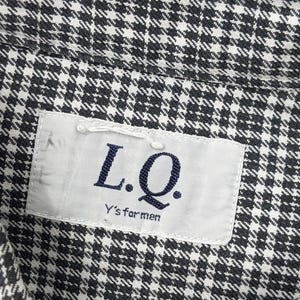 Puede incluir: Primer plano de una camisa con estampado de pata de gallo en blanco y negro. La camisa tiene una etiqueta que dice "L.Q. Y's for men". La tela est&aacute; tejida de forma apretada, creando una apariencia texturizada. La est&eacute;tica general es cl&aacute;sica y vers&aacute;til.