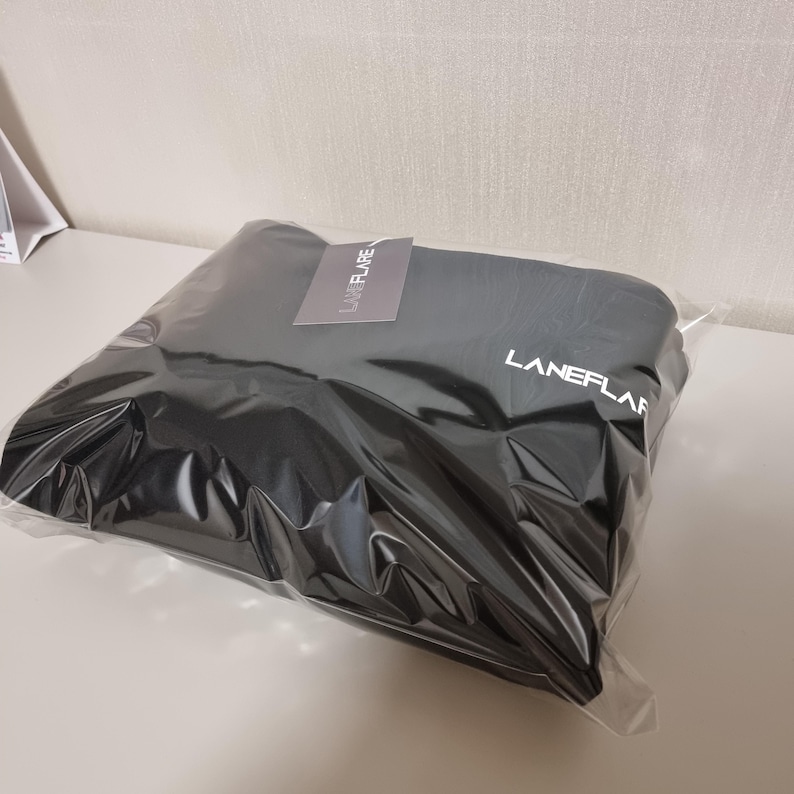 May include: A folded black garment packaged in a clear plastic bag. The item features the white text LANEFLARE printed on the fabric and includes a small grey tag with the same brand name LANEFLARE attached to the top of the plastic packaging.