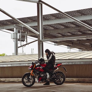 May include: A red and black sport motorcycle with gold front forks and a black exhaust pipe. A person wearing a black hooded sweatshirt and black pants is seated on the motorcycle. The text DUKE_.PICS and @sasha.gzl appear at the bottom.