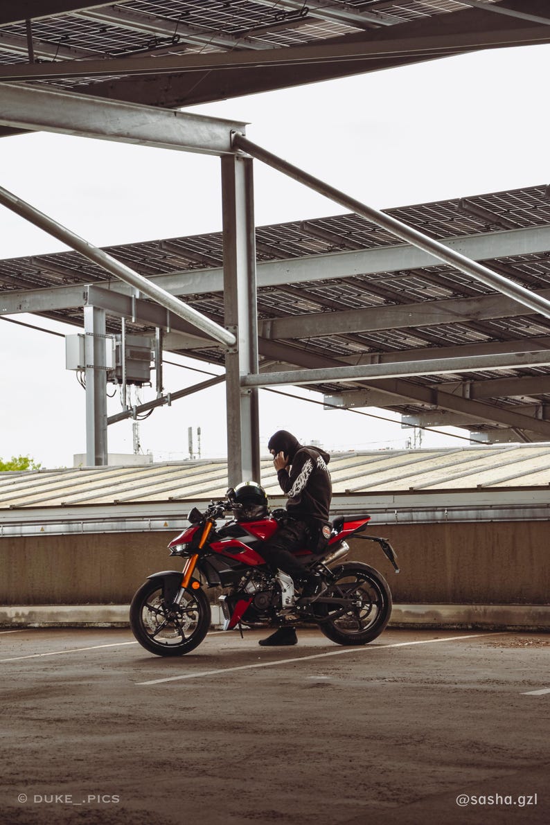 May include: A red and black sport motorcycle with gold front forks and a black exhaust pipe. A person wearing a black hooded sweatshirt and black pants is seated on the motorcycle. The text DUKE_.PICS and @sasha.gzl appear at the bottom.