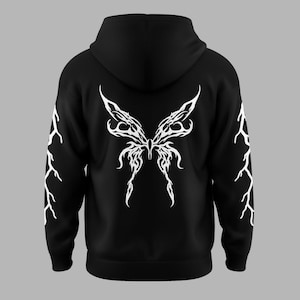 Puede incluir: Sudadera con capucha negra con un dise&ntilde;o de alas de mariposa blancas en la espalda. Las mangas presentan patrones de rayos blancos. La sudadera tiene capucha y un corte holgado.