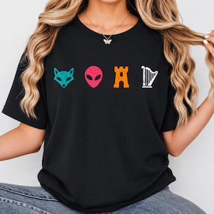 Op de afbeelding: Zwart T-shirt met vier kleurrijke grafische iconen: een turquoise vossenkop, een roze alienhoofd, een oranje kasteel en een witte harp. Het shirt is gemaakt van een zacht materiaal.