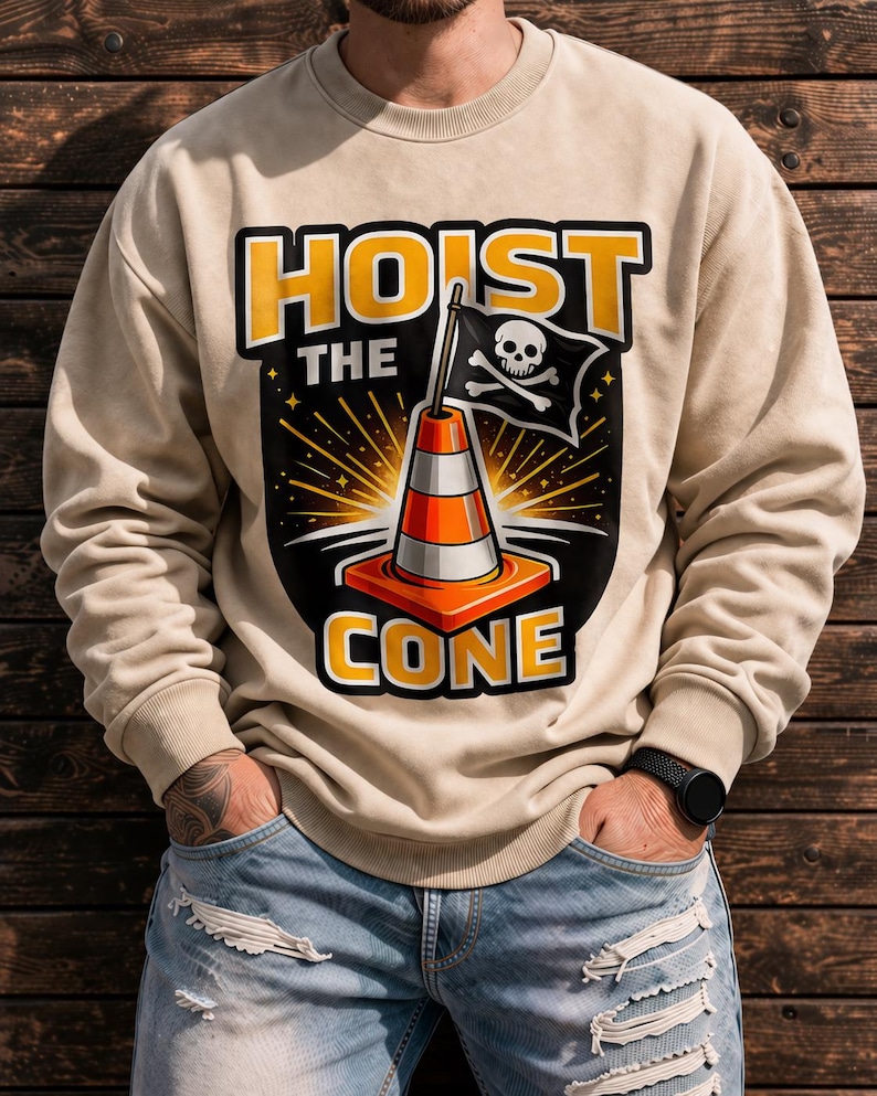 May include: Beige sweatshirt with the words "HOIST THE CONE" in yellow and black. The graphic features a traffic cone with a skull and crossbones flag. The sweatshirt is worn with blue jeans.