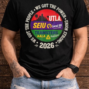 May include: Black t-shirt with a circular graphic featuring text and a skyline silhouette. The graphic includes the words "WE GOT THE PEOPLE" and "WE GOT THE POWER". Other text includes "UTLA", "SEIU Local 99", "TEAMSTERS AALA Local 2010", and "2026".