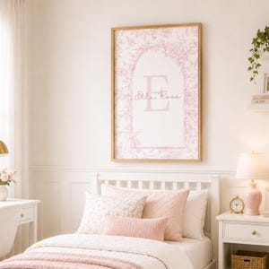 May include: A rectangular wall art print in a light wood frame featuring a pink and white floral toile pattern. The design includes a central archway containing a large capital letter E and the name Ella Rose in a cursive script font.