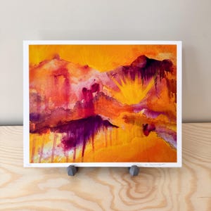 May include: An abstract watercolor painting with a vibrant color palette. The artwork features a landscape with mountains in shades of orange, yellow, red, and purple. The sun is depicted with bright yellow rays. The painting is displayed on a white background.