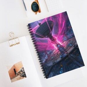May include: Spiral-bound notebook featuring a futuristic illustration of a satellite dish and a complex structure with vibrant pink and blue energy effects. The notebook is open on a white surface, with a gold paper clip and sunglasses.