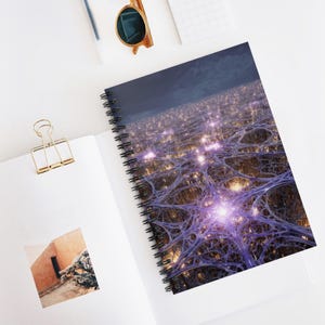 May include: Spiral-bound notebook featuring a vibrant, abstract design with a network of blue lines and glowing purple and gold lights. The notebook is open on a white surface, with a gold paper clip and sunglasses nearby.