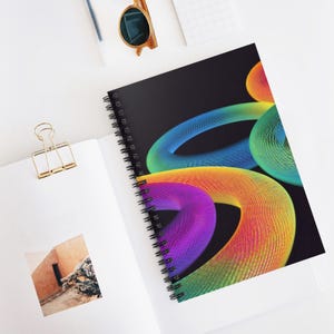 Pode incluir: Um caderno espiralado com uma capa preta com um design abstrato vibrante de formas coloridas do arco-íris entrelaçadas. O caderno está aberto, revelando páginas brancas. Óculos de sol e um clip de papel dourado também são visíveis.