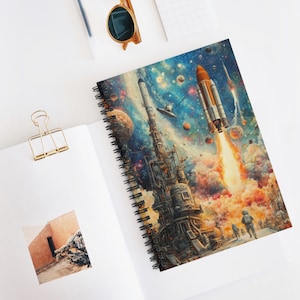 May include: Spiral-bound notebook featuring a vibrant space-themed illustration. The artwork depicts rockets, planets, and astronauts against a colorful nebula backdrop. The notebook is open, revealing the detailed cover art and a glimpse of the blank pages.