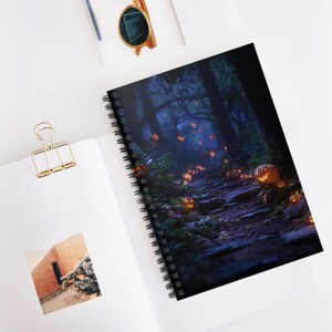 May include: A spiral-bound notebook featuring a Halloween-themed forest scene with carved pumpkins lining a path. The cover art depicts a dark, mysterious forest with glowing jack-o'-lanterns, creating a spooky atmosphere. The notebook is open on a white surface.