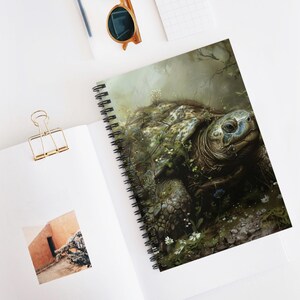 May include: Spiral-bound notebook featuring a detailed illustration of a tortoise covered in foliage. The artwork showcases a realistic depiction of the tortoise's shell and face, with a serene, naturalistic background. The notebook is open on a white surface.