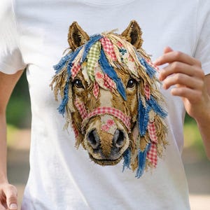 May include: White t-shirt featuring a detailed illustration of a horse's head. The horse has a brown face, with colorful fabric accents in its mane and a red and white checkered halter. The design is centered on the shirt.