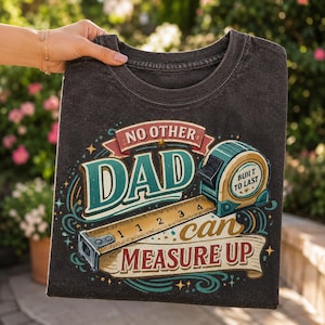 May include: A charcoal grey t-shirt featuring a graphic print of a tape measure and the text "NO OTHER DAD can MEASURE UP" and "BUILT TO LAST". The design includes decorative swirls and stars in shades of teal, red, and cream on the front.