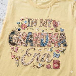 Puede incluir: Camiseta amarillo claro con la frase bordada "IN MY GRANDMA Era". El diseño incluye letras de patchwork, estampados florales, botones y elementos decorativos como mariposas y corazones.