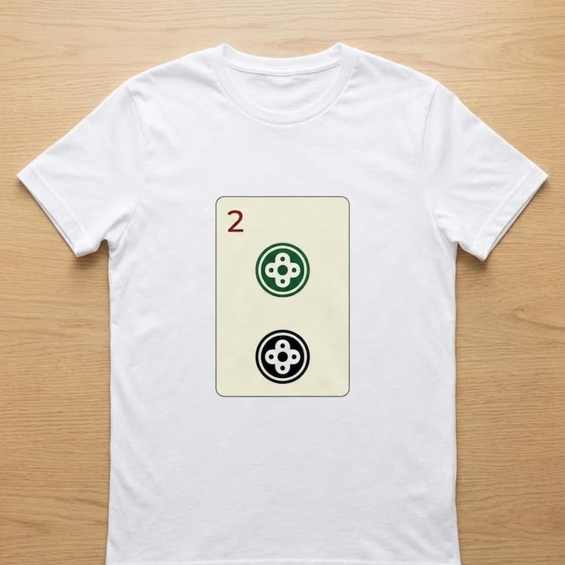 Puede incluir: Camiseta blanca con un dise&ntilde;o de carta de juego. La carta tiene un fondo beige con el n&uacute;mero "2" en rojo en la parte superior. Debajo, dos s&iacute;mbolos estilizados en forma de tr&eacute;bol, uno verde y otro negro.