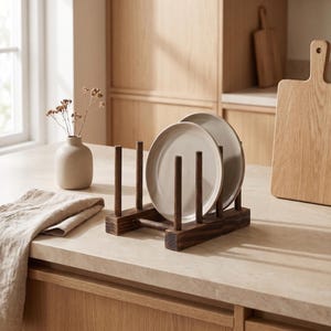 Può includere: Uno scolapiatti in legno marrone scuro che sostiene due piatti rotondi in ceramica color beige chiaro. Il supporto presenta una base rettangolare con pioli verticali disposti in modo da mantenere i piatti in posizione verticale.