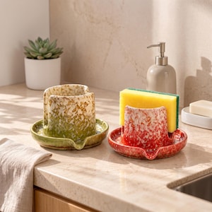 Peut inclure: Deux porte-éponges en céramique avec égouttoirs intégrés. L'un présente une finition tachetée verte et blanche, tandis que l'autre est tacheté rouge et blanc et contient une éponge rectangulaire jaune avec une couche abrasive verte.