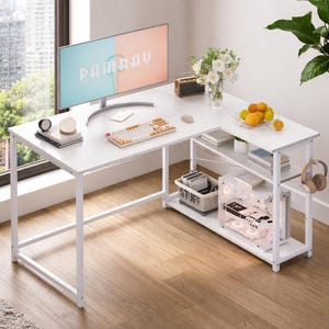 May include: White L-shaped computer desk with a metal frame. The desk has a monitor with the word "PAMRAV" on the screen, a keyboard, and a shelf for storage. A basket, books, and a computer tower are visible.