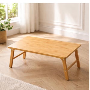 May include: A rectangular, light-brown bamboo laptop table with folding legs. The table is approximately 24 inches long, 16 inches wide, and 8 inches high when the legs are extended. The table is set on a light-colored wooden floor.