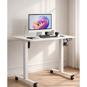 May include: A white adjustable-height desk with a computer monitor, keyboard, mouse, and headphones. The desk has a minimalist design with a rectangular tabletop and four rolling wheels. A black coffee mug and a small speaker are also on the desk.