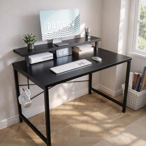 May include: A black computer desk with a raised shelf, featuring a computer monitor, keyboard, and mouse. A small plant and digital clock are on the shelf. Headphones hang from the side.