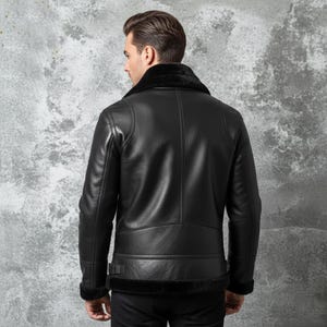 May include: Black leather jacket with a shearling collar and trim. The jacket has a classic aviator style with a belted waist and cuffs. The back view shows the jacket's details, including the stitching and paneling.