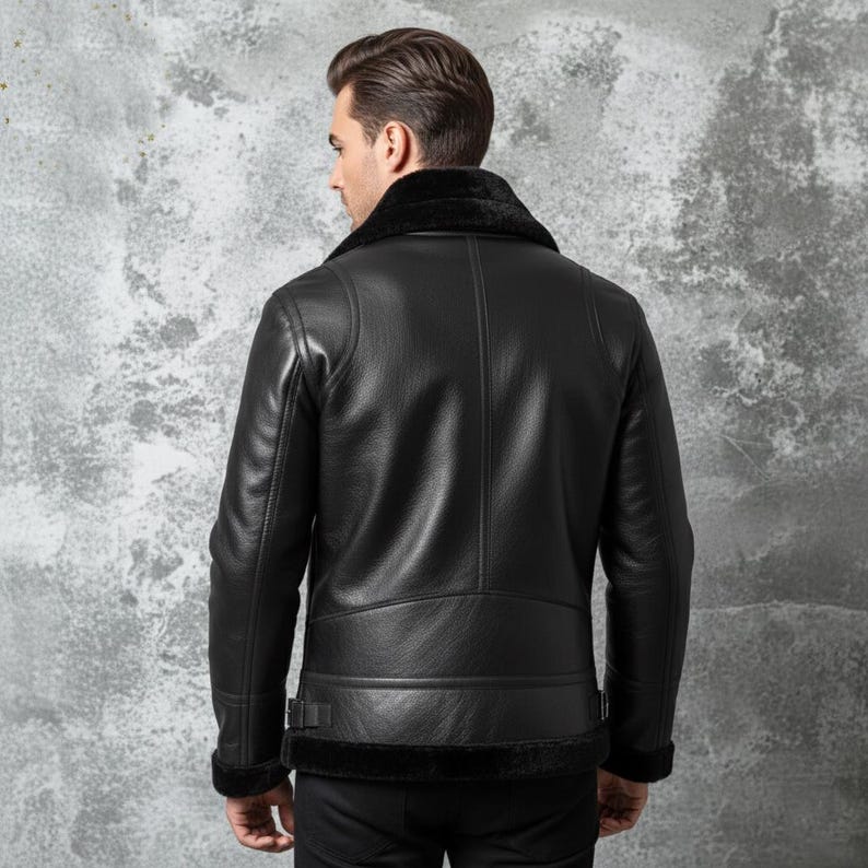 May include: Black leather jacket with a shearling collar and trim. The jacket has a classic aviator style with a belted waist and cuffs. The back view shows the jacket's details, including the stitching and paneling.