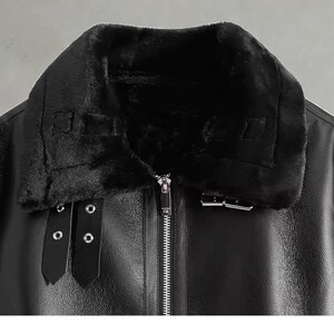 May include: Black faux leather jacket with a plush, black faux fur collar. The jacket features a full-length zipper, two buckle straps, and a buckle closure. The jacket is a close-up shot, showcasing the details of the design.