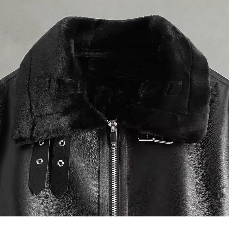 May include: Black faux leather jacket with a plush, black faux fur collar. The jacket features a full-length zipper, two buckle straps, and a buckle closure. The jacket is a close-up shot, showcasing the details of the design.