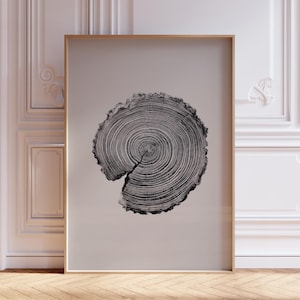 May include: A framed monochrome print of a tree trunk cross-section. The image shows detailed growth rings and a central split. The print is set in a gold-coloured frame against a neutral backdrop.